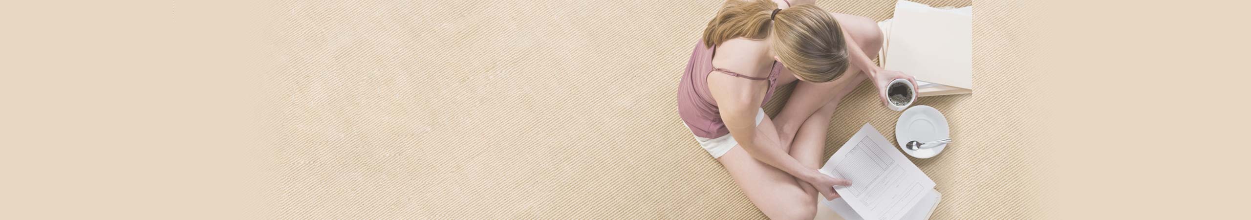 Woman sitting on her carpeted floor drinking coffee and reading some documents