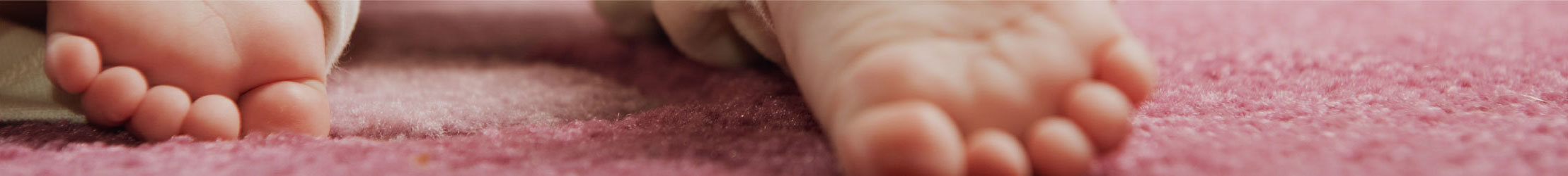Close up of a babies feet resting on some pale pink carpet